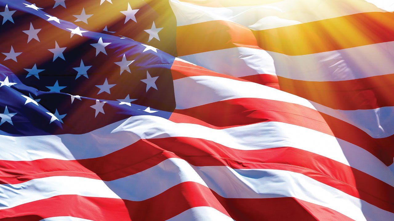 american flag waving in the wind with sun shining down