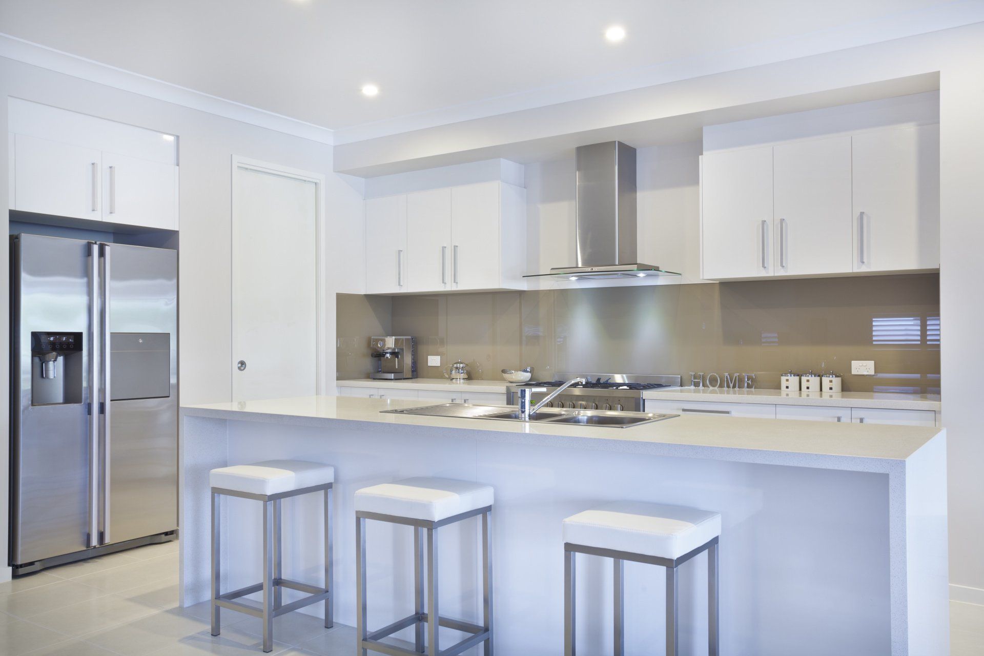 A kitchen with white cabinets and stools and a refrigerator