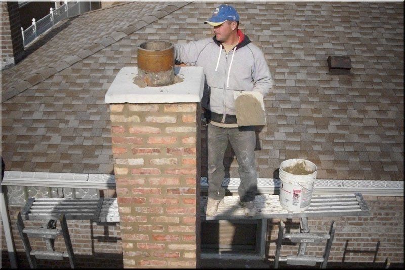 A man is working on a brick chimney on a roof