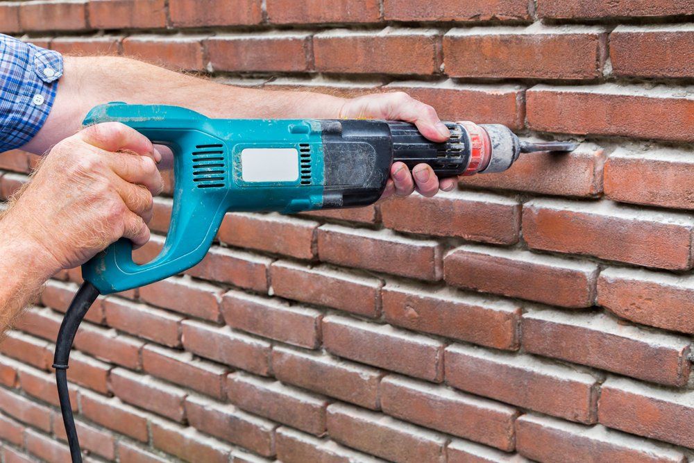 A man is using a drill to drill a hole in a brick wall.