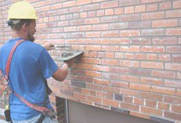 A man wearing a hard hat is working on a brick wall.