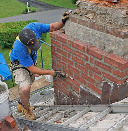 A man in a blue shirt is working on a brick chimney