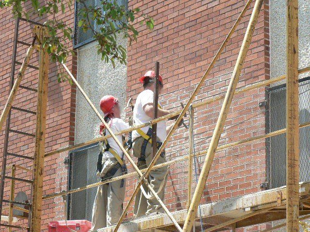 Two construction workers are working on a brick building on a scaffolding.