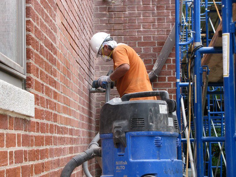 A man wearing a hard hat is using a blue vacuum cleaner on a brick wall