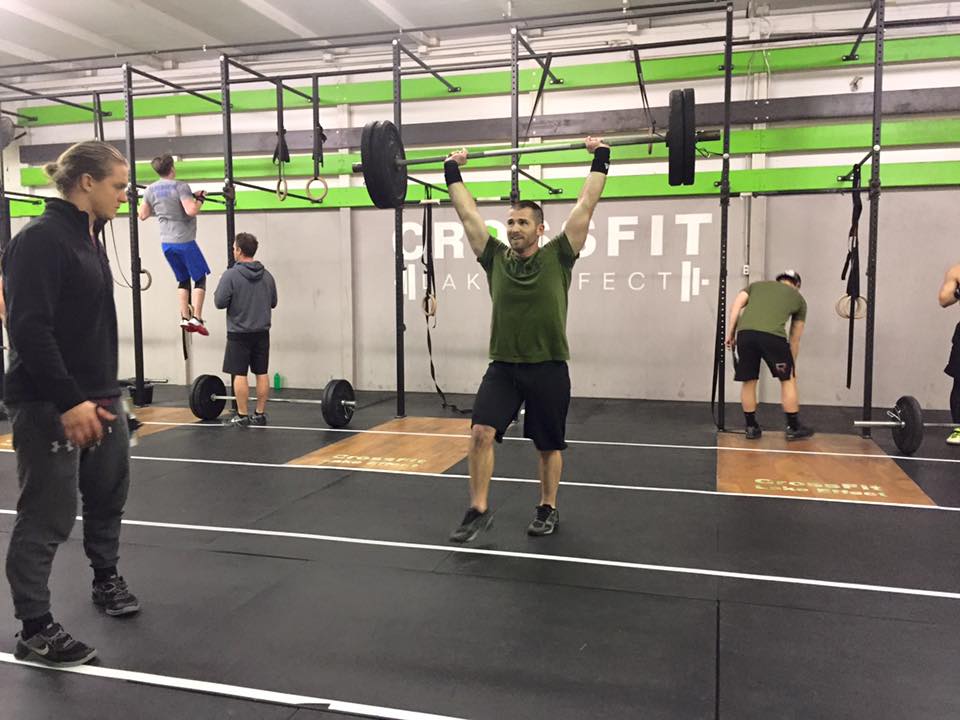 A man is lifting a barbell over his head in a gym.