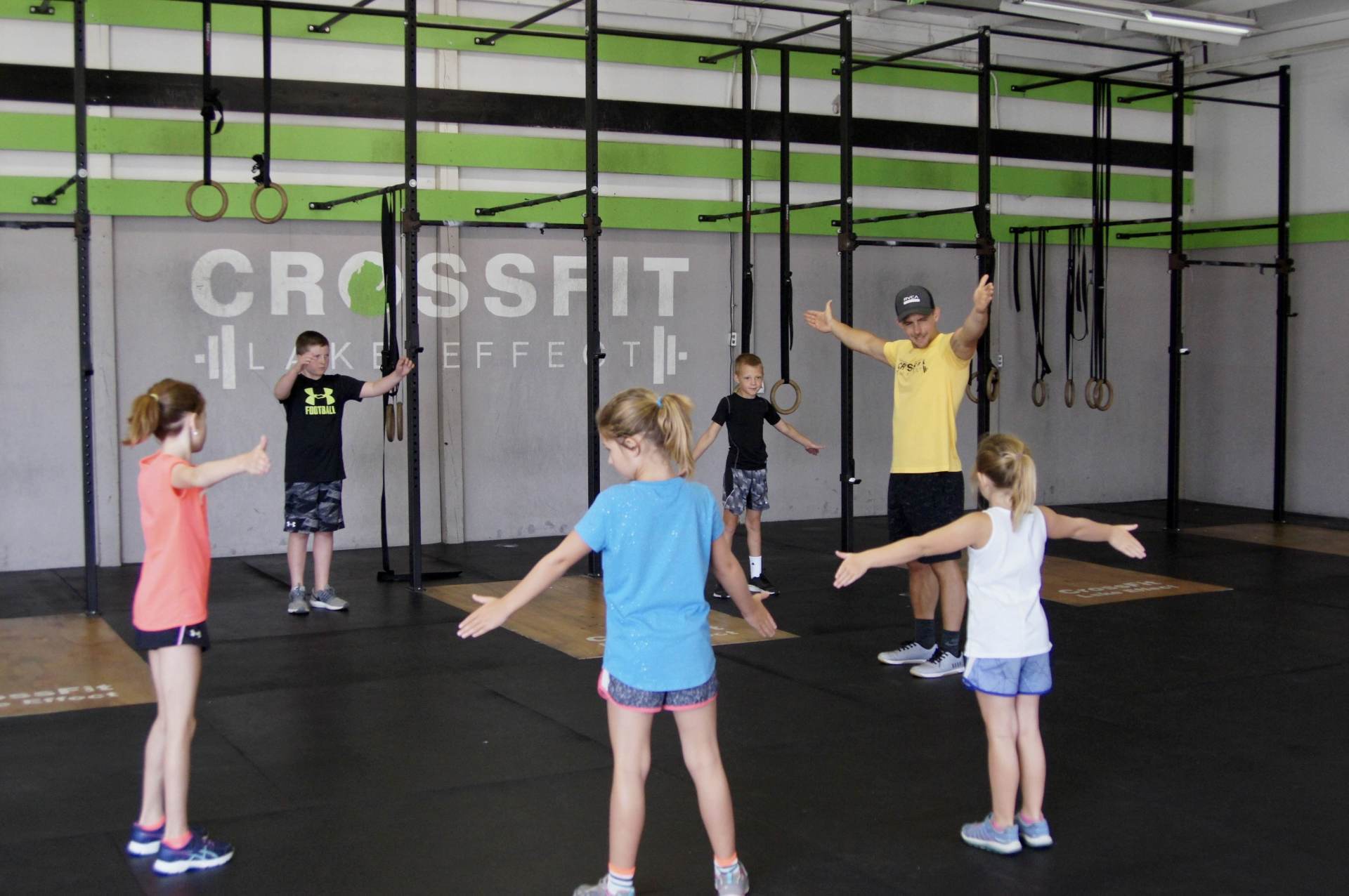 A group of children are standing in a gym with their arms outstretched.