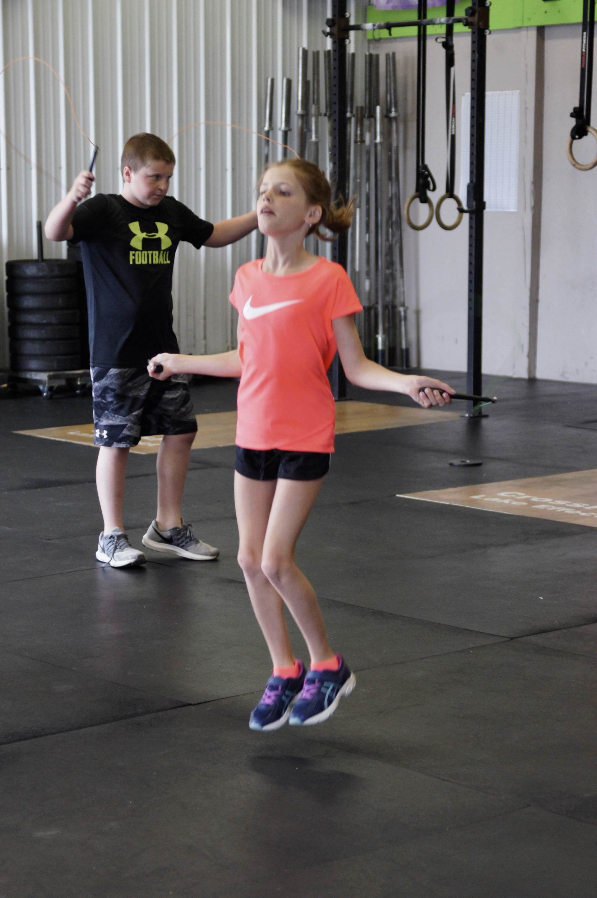 A boy and a girl are jumping rope in a gym.