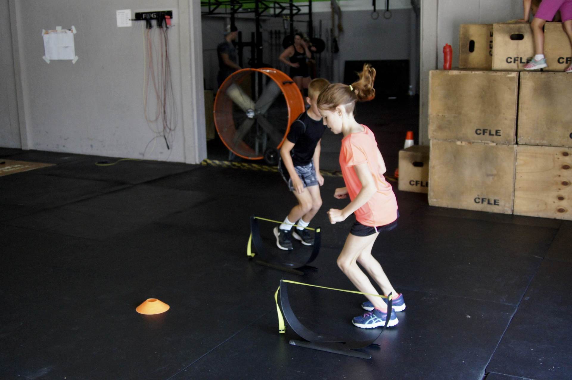 Two young girls are jumping over hurdles in a gym.