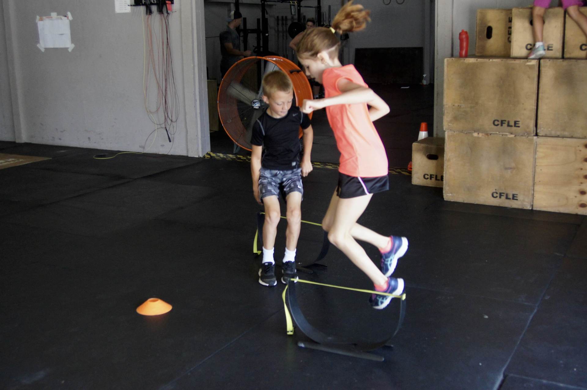 A boy and a girl are jumping over a hoop in a gym.