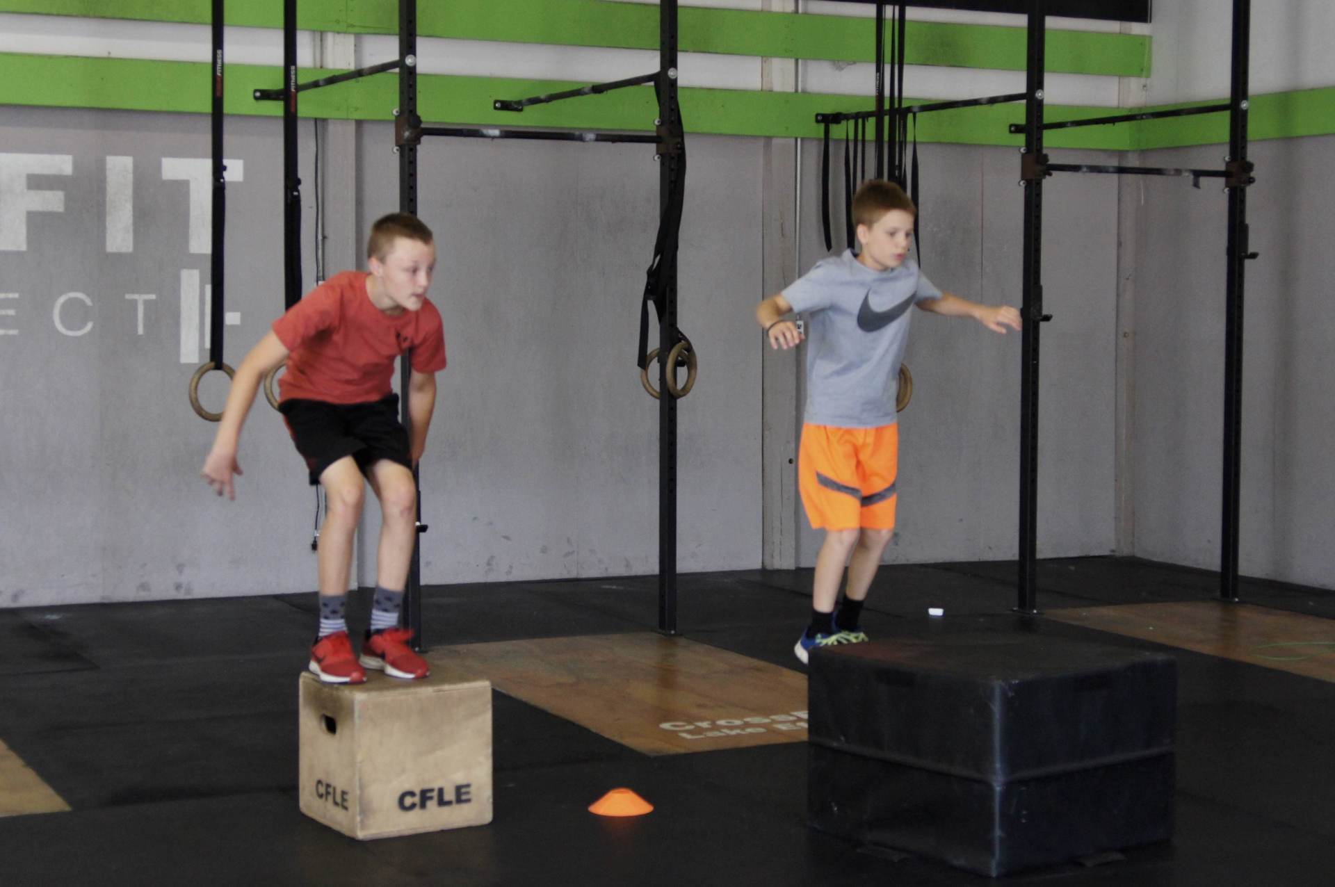 Two young boys are jumping on boxes in a gym.