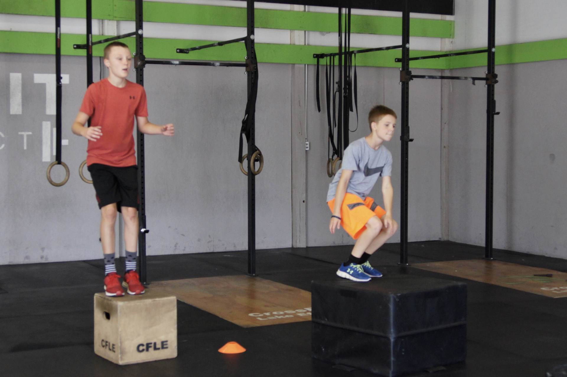 Two young boys are jumping on a box in a gym.