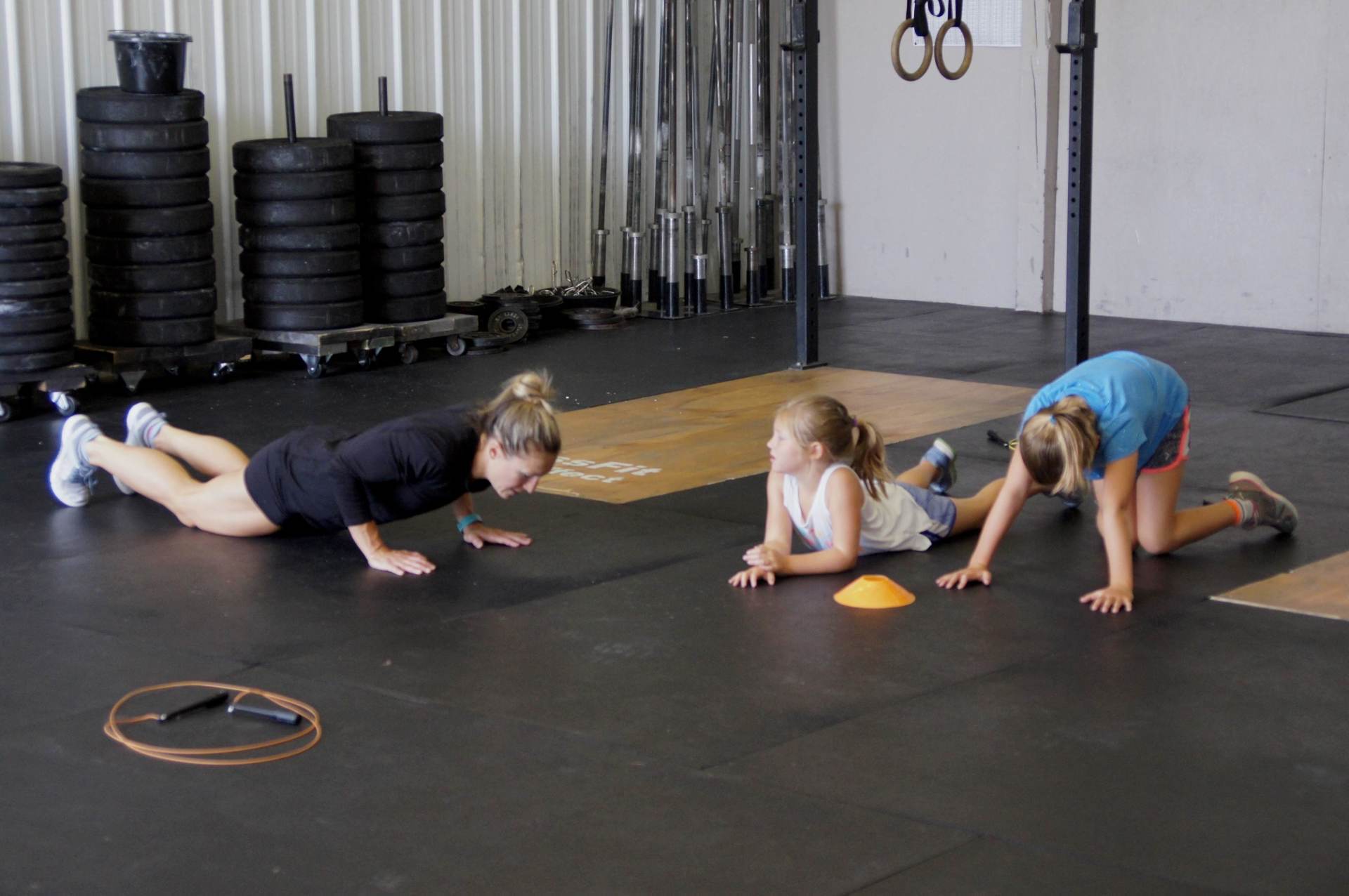 Three young girls are doing push ups on the floor in a gym.