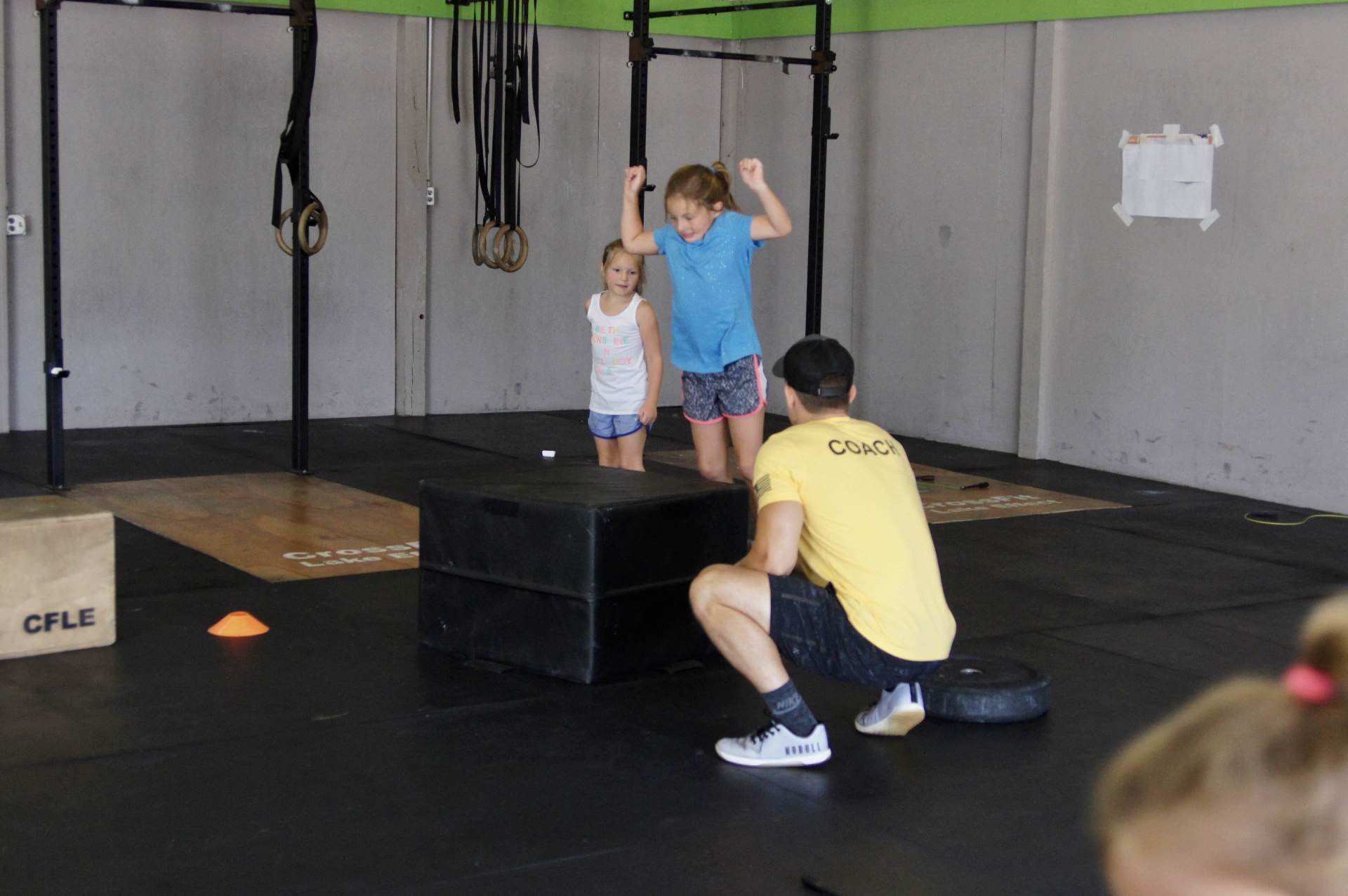 A man in a yellow shirt is kneeling down next to two children in a gym.