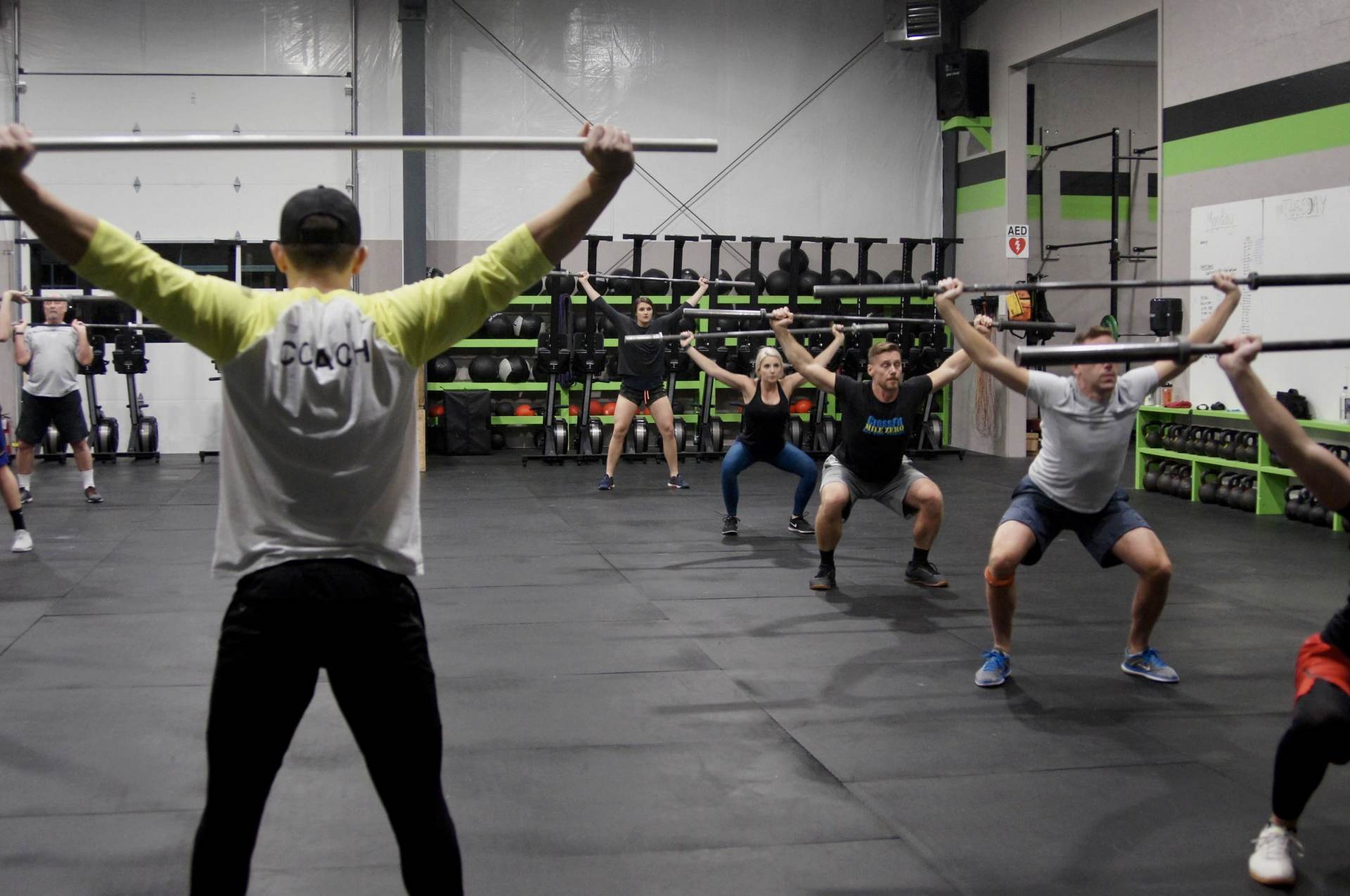 A group of people are doing squats with barbells in a gym.