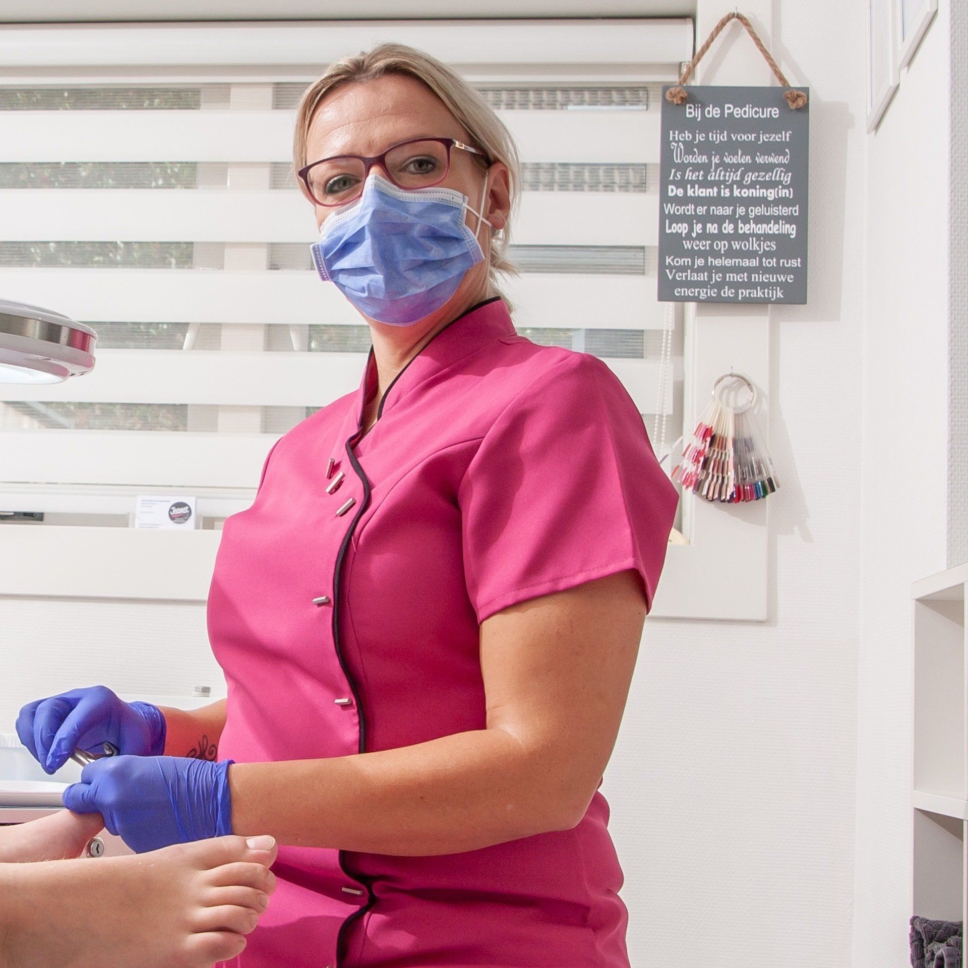 Een zorgmedewerker in roze uniform en met mondkapje helpt een patiënt tijdens een handbehandeling.