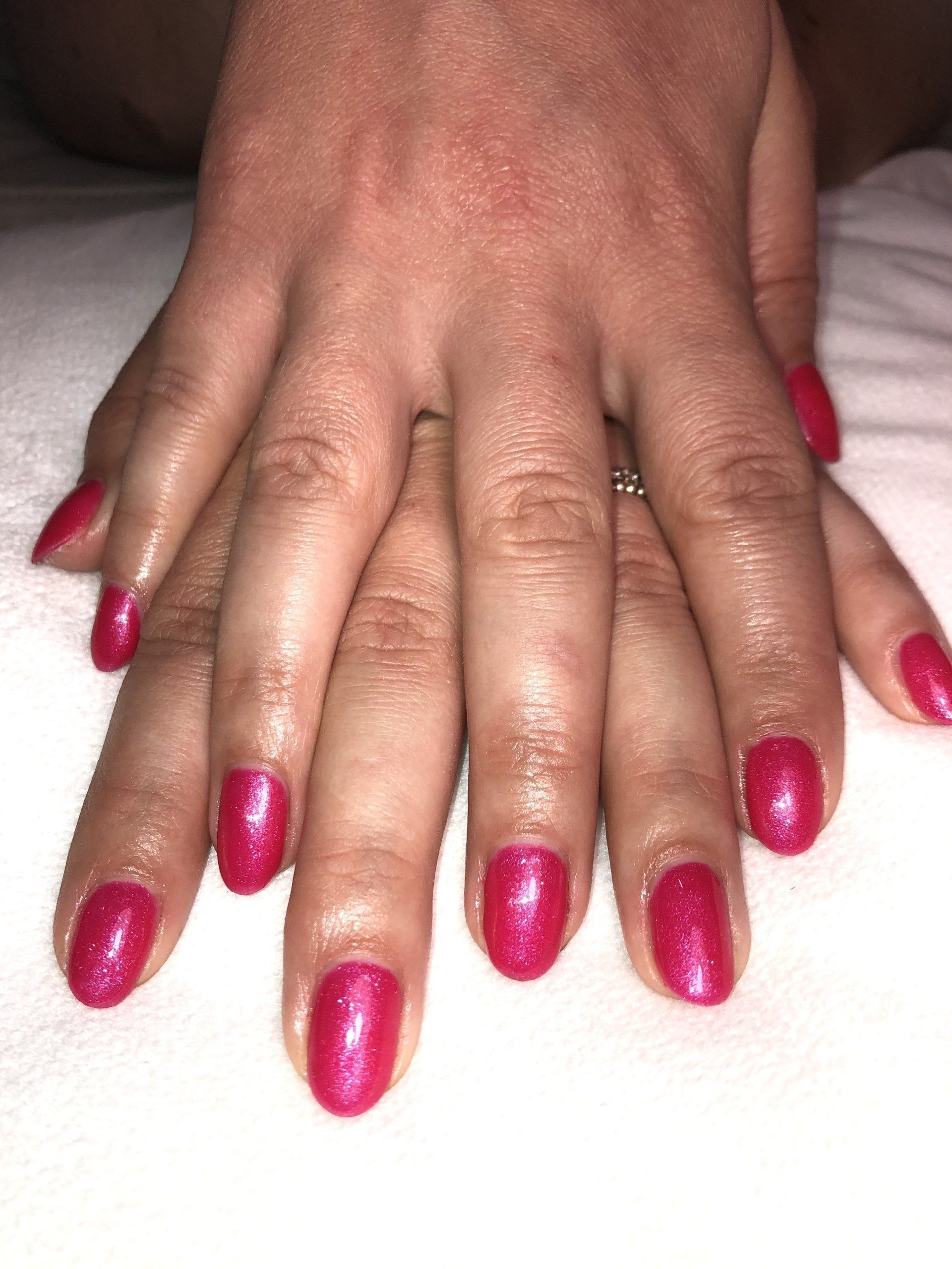 Handen met felroze glitternagels rusten op een witte ondergrond.