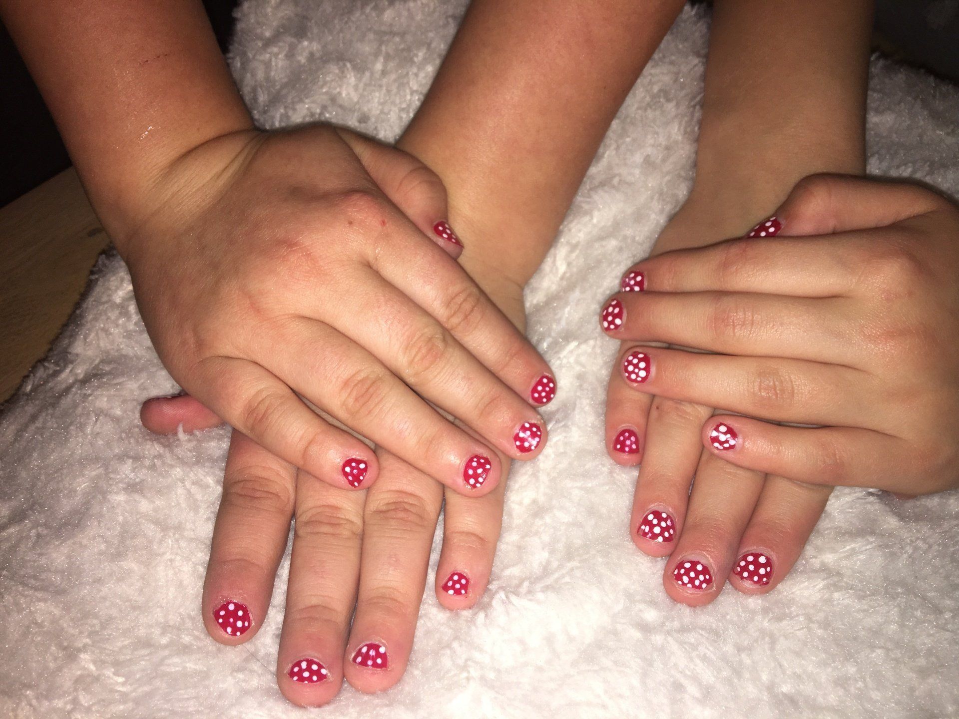 Drie handen met roze glitterlak rusten op een witte, pluizige deken.