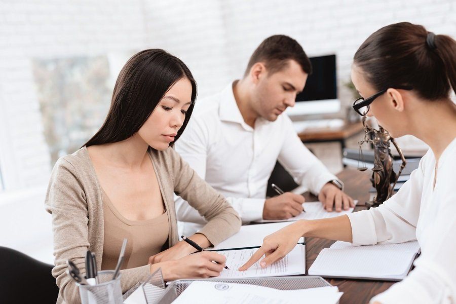 a man and woman signing divorce papers while being guided by a professional attorney