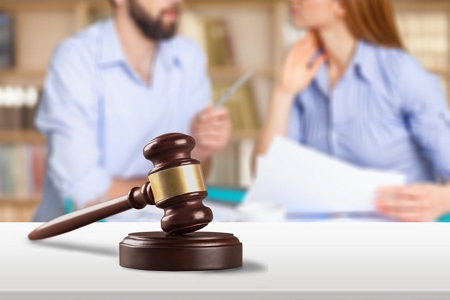 a gavel resting against a sound block with a blurred image of two clients in the background