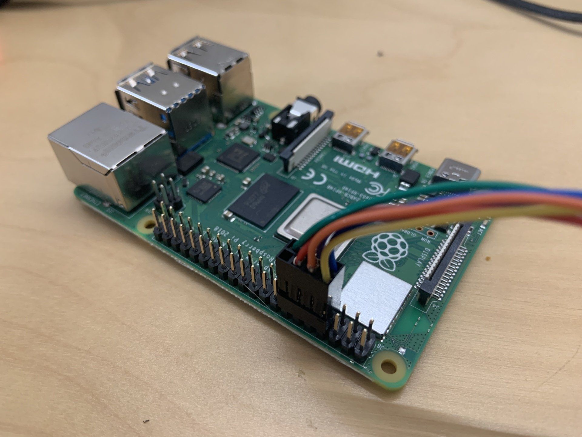 A green Raspberry Pi single-board computer resting on a desk with a multi-colored jumper wire connector attached to pins.