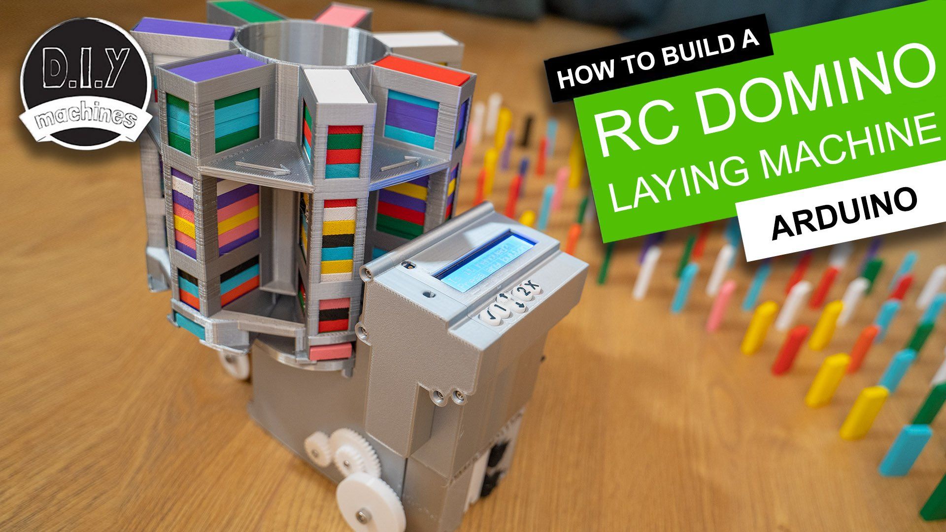 A DIY 3D-printed RC domino-laying machine on a wooden floor, next to a line of colorful standing dominoes.