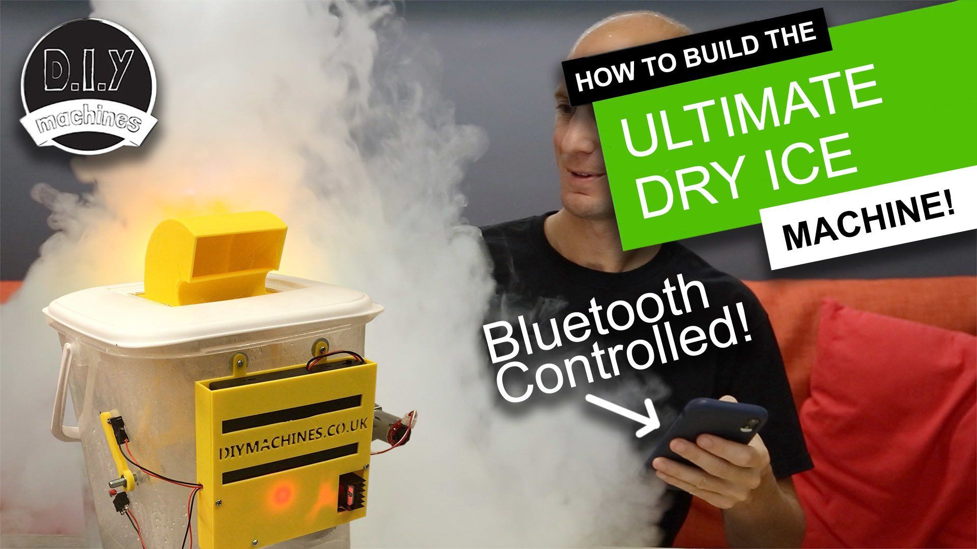 A man uses a phone to control a DIY machine producing thick dry ice fog, labeled for a video on how to build the device.