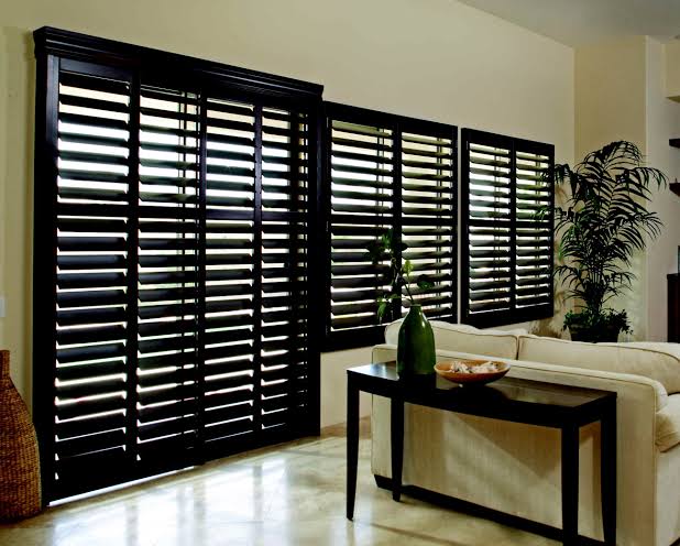 Dark wooden shutters on windows and a sliding glass door in a living room.