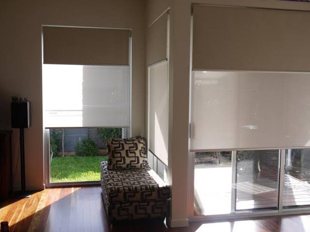 Interior room with beige roller blinds, a patterned chaise lounge, and a view of a yard through windows.