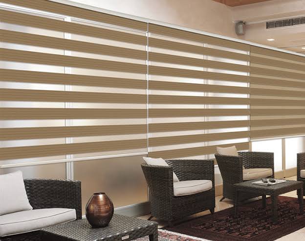 Beige and tan zebra blinds on glass windows, covering seating area with rattan furniture.