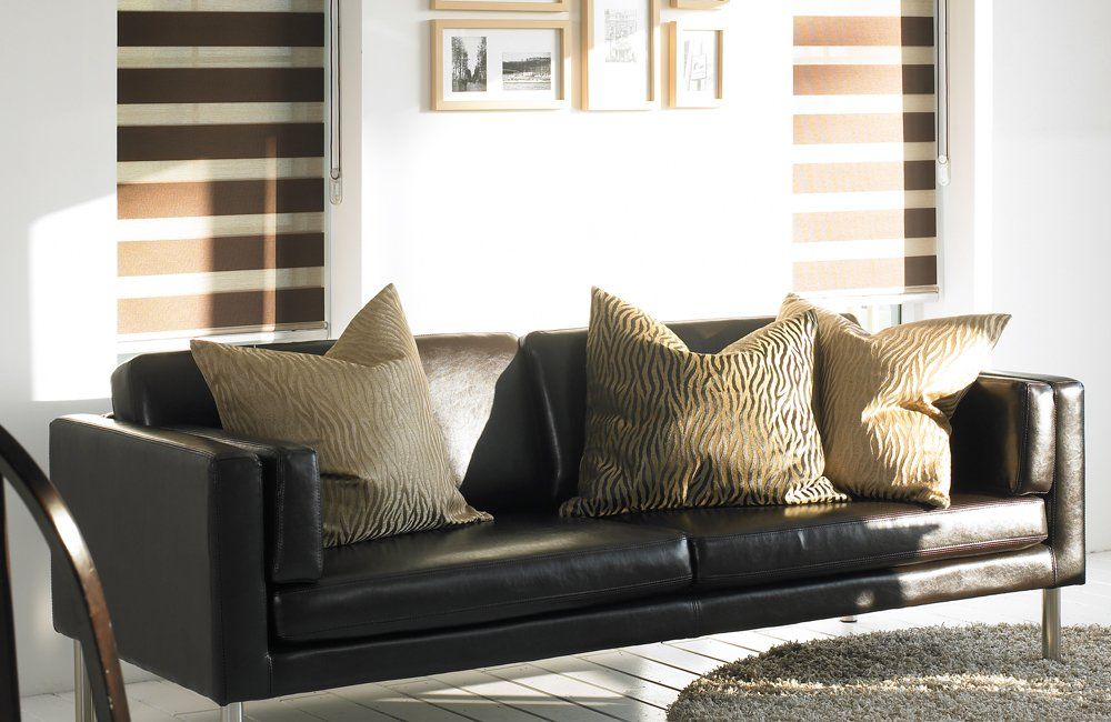 Black leather sofa with gold pillows, near a window with striped blinds.