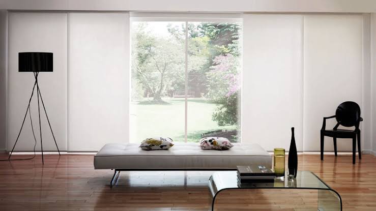 Modern living room with sheer white sliding panel curtains, minimalist furniture, and a view of a garden.