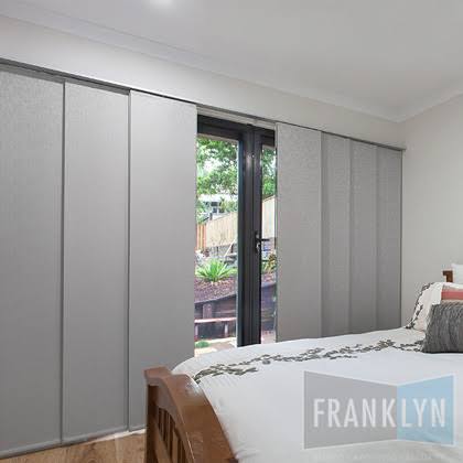 Bedroom with gray panel blinds covering a sliding glass door, a bed in the foreground.