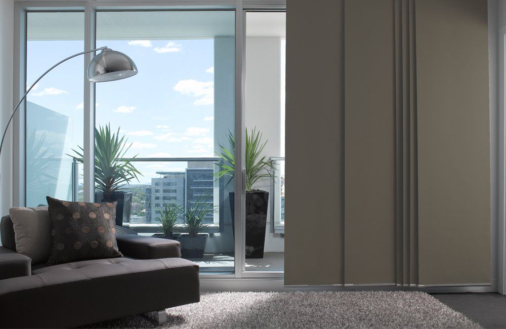 Living room with sliding door leading to balcony, vertical blinds, modern decor, and outdoor plants.