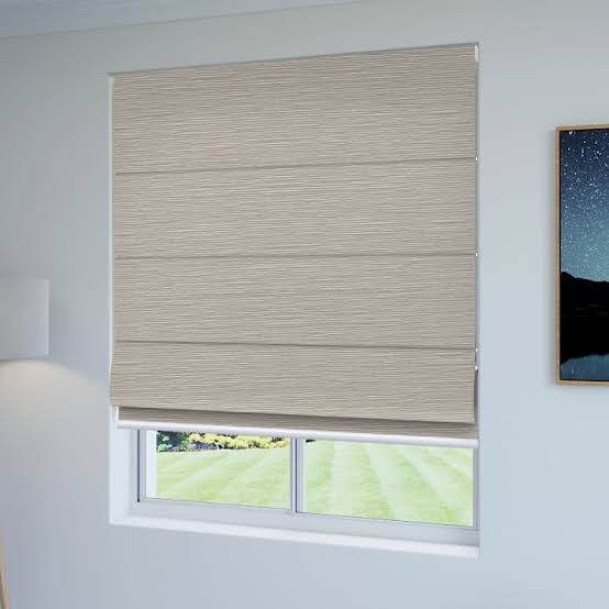 Beige Roman shade covering a window, with a view of a green lawn outside.