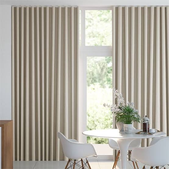 Beige curtains frame a window overlooking greenery; a table and chairs are in front.