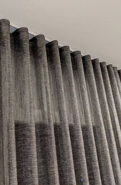 Gray, textured curtains hanging from a ceiling track, creating vertical folds.