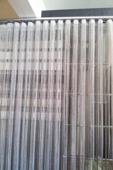Rows of thin, white fibers hanging vertically from a metal structure, possibly a textile process.