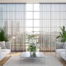 Living room with sheer curtains, city view, two sofas, coffee table, and plants.