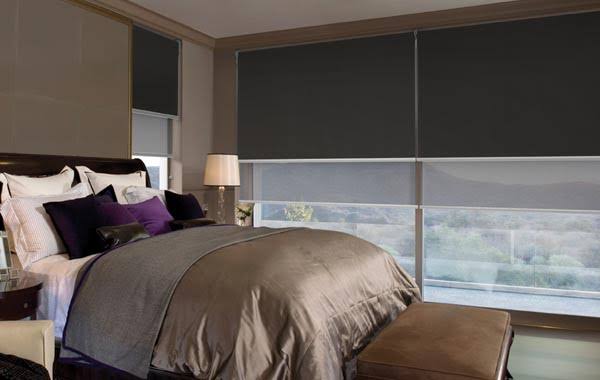 Bedroom with a bed and dark gray window shades partially covering a large window.