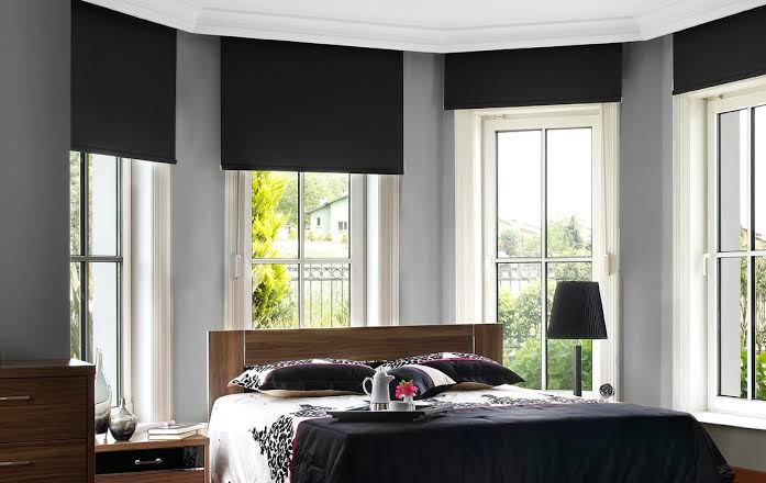 Bedroom with black shades on windows, wooden bed, nightstand, dresser.