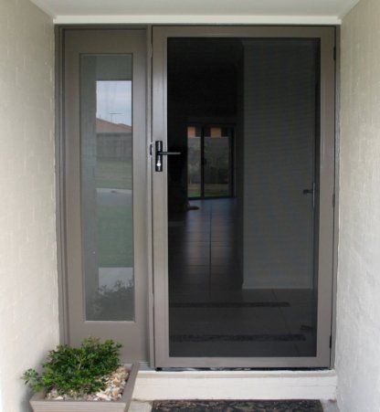 Exterior view of a house entry with a screen door and sidelight. Gray door, light walls, and a small potted plant.