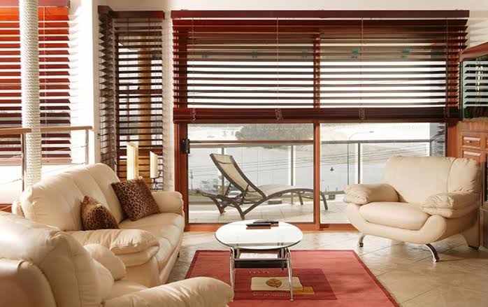 Living room with cream-colored sofas, wooden blinds, and a view of a waterfront.