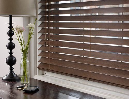Dark wooden blinds on a window, a table with a lamp, flowers, keys, and a phone.