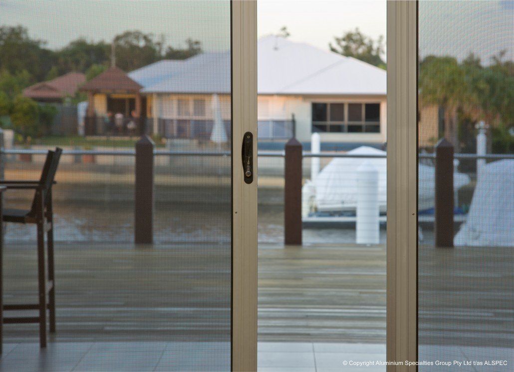 Sliding glass door open onto a waterside deck; buildings and a boat are visible in the background.