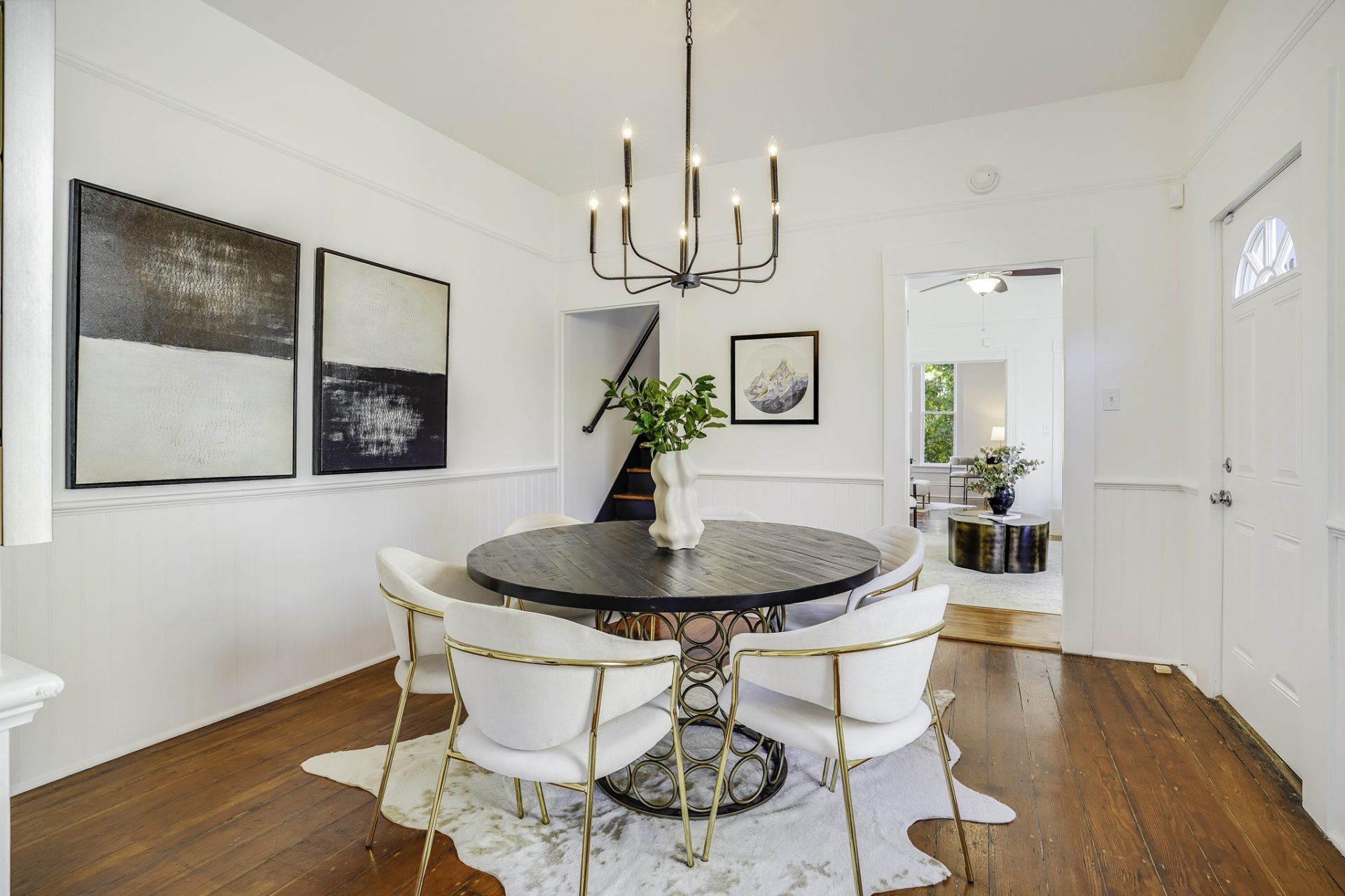 Dining room with round black table, white chairs, and black chandelier.