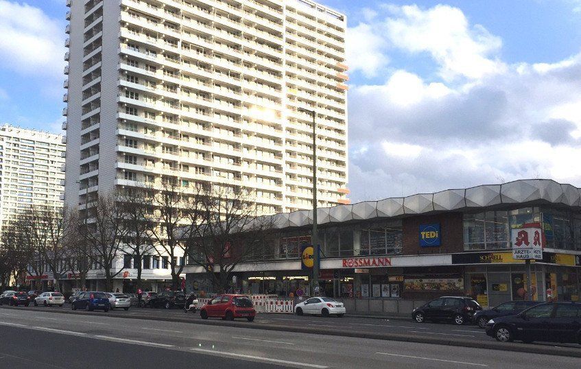 市街地の通り沿いにある、リドル スーパーマーケットを含む一列の商店の隣に建つ高層マンション。