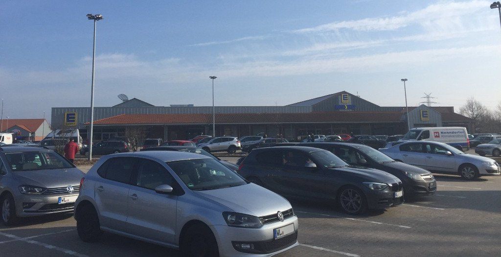 Parking lot with cars in front of a supermarket building under a clear blue sky.