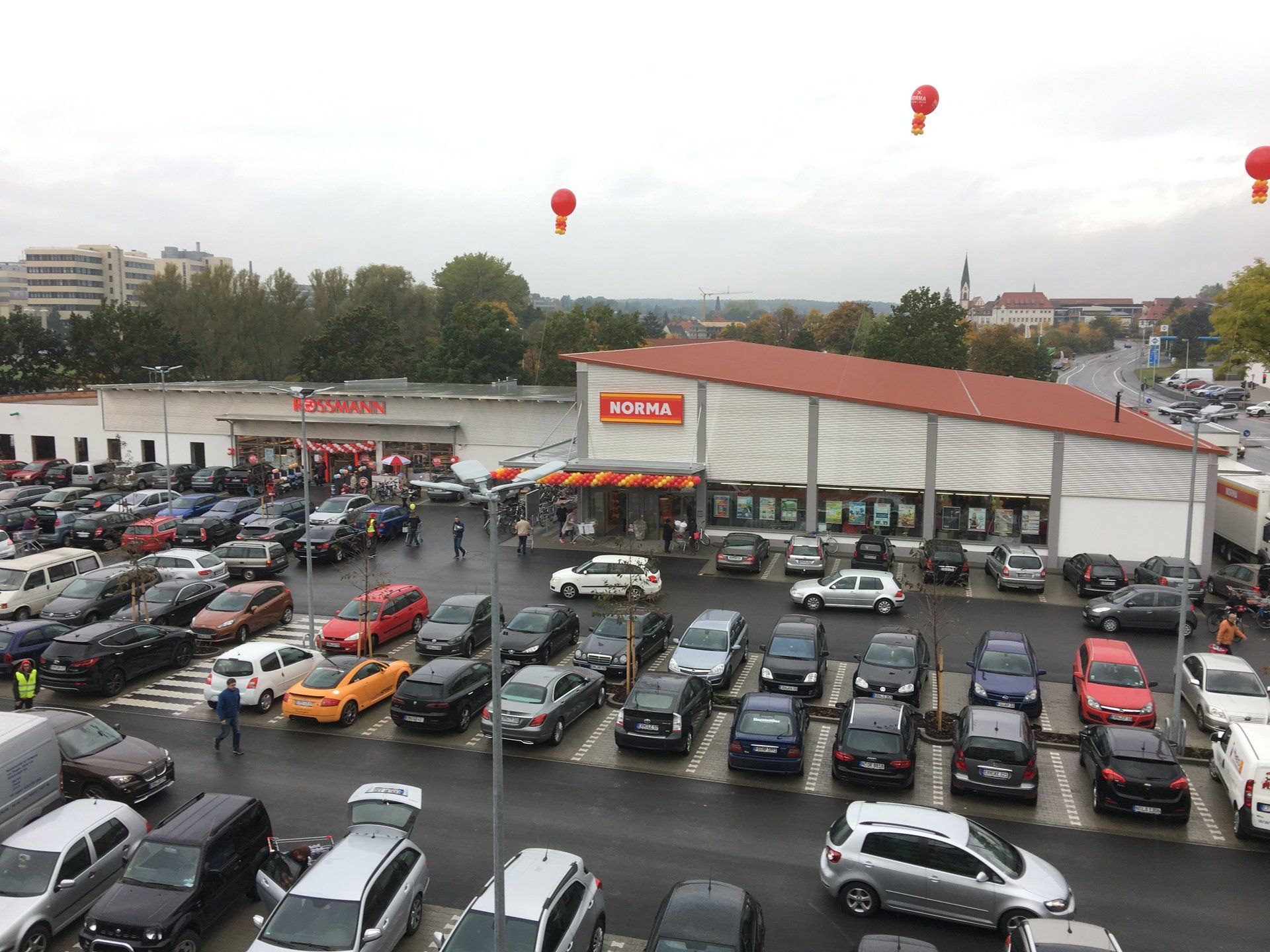 駐車場が満杯で、空には赤い風船が浮かぶ REWE スーパーマーケットの外観。
