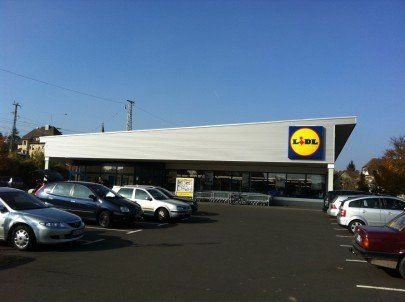 Sklep spożywczy Lidl z zaparkowanymi samochodami przed nim w słoneczny dzień.