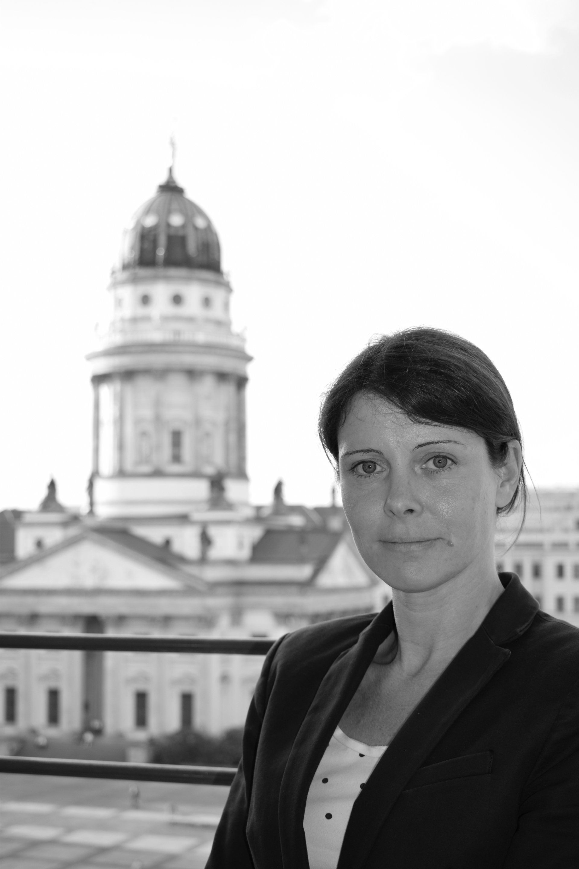 Žena v saku, v pozadí budova s ​​kupolí.